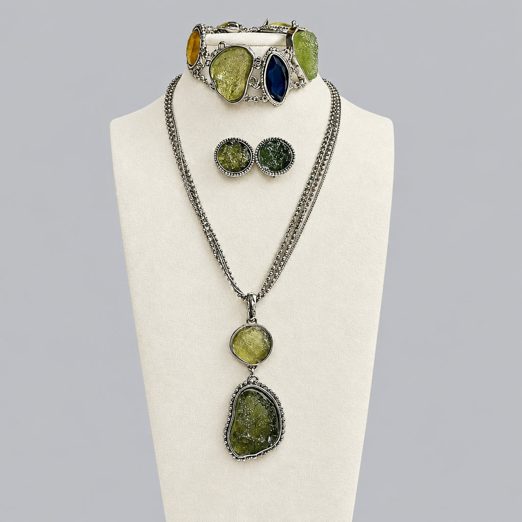 A jewelry set displayed on a cream mannequin bust, featuring a silver-tone chain necklace with three large natural green stones, matching round stud earrings, and a wide silver-tone cuff bracelet with green and blue stones.