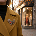 Vintage-inspired owl brooch pin with open wings, bronze detailing, and amber glass accents, pinned on a woman's brown jacket.