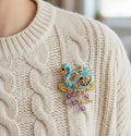 Decorative brooch shaped like a swan with gold and purple accents pinned on a ivory sweater