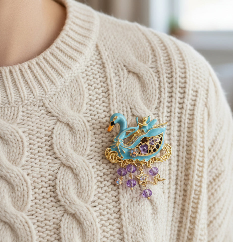 Decorative brooch shaped like a swan with gold and purple accents pinned on a ivory sweater