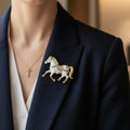 Decorative horse brooch with gold and white details, pinned on a blue suite