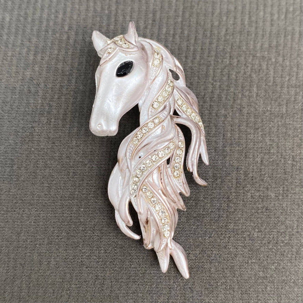 Decorative horse head brooch with intricate details on a gray background