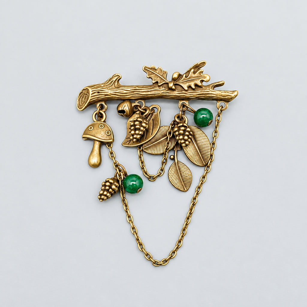 Woodland mushroom charm brooch with bronze-tone leaves, acorns, green beads, and dangling chains against a gray background.